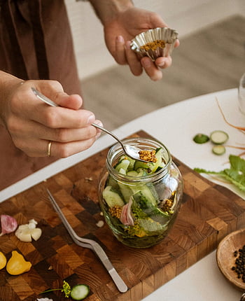 pickled vegetables, cucumbers, garlic, kitchen setting, hands preparing, silver spoon, chickpeas, jar, cutting board, food preparation, vegetables