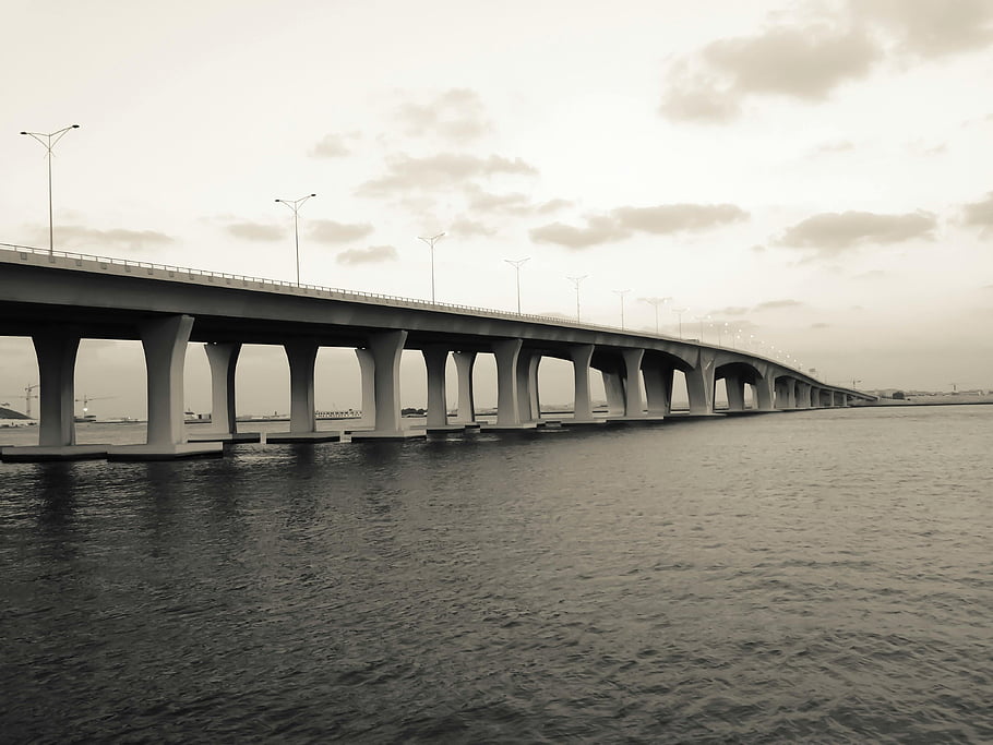 white and gray bridge, body of water, serene waters, cloudy sky, sepia tone, sleek bridge, bridge over water, architectural photography, landscape photography, urban infrastructure, waterway crossing