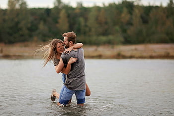 man hugging woman, laughing woman, standing in water, young couple, joyfully playing, natural backdrop, love and happiness, couple in water, outdoor couple, romantic moment, playful couple