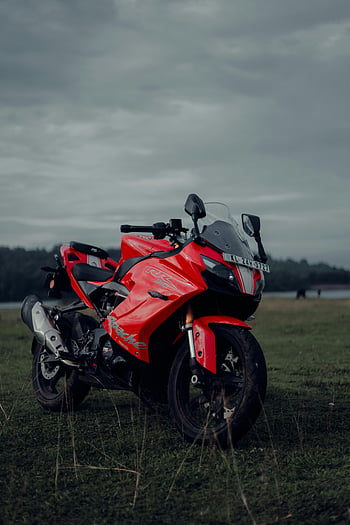 Red TVS Apache RR 310, vibrant red motorcycle, lush grass, overcast Kerala backdrop, parked motorcycle, TVS Apache, RR 310, Kerala landscape, outdoor motorcycle, red sports bike, green field