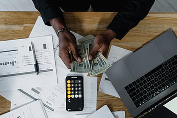 Počítání amerických dolarů, finanční dokumenty, dřevěný stůl, kalkulačka, laptop, Počítání člověka, Správa peněz, finanční plánování, kancelářská práce, podnikové finance, Manipulace s hotovostí