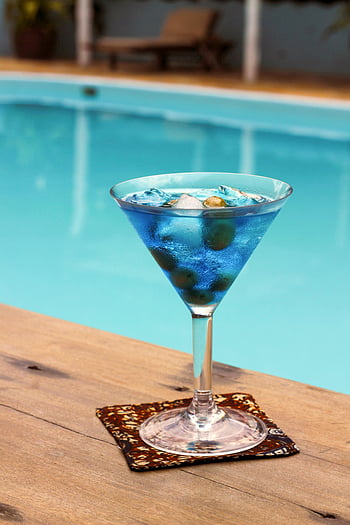 blue cocktail, swimming pool, summer relaxation, liquid in glass, poolside drink, cool beverage, outdoor refreshment, martini glass, ice cubes, poolside setting, summer drink