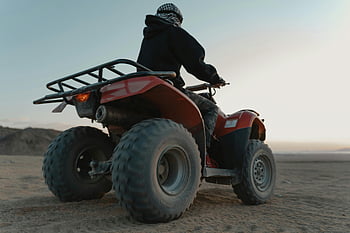 Man riding ATV, red ATV, gray sand, desert adventure, quad bike, dawn scene, thrill ride, off-road vehicle, desert landscape, adventure sport, man on ATV