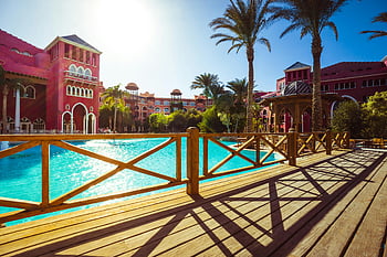 tropical resort, luxurious poolside, palm trees, vibrant architecture, ultimate relaxation, pink house, stunning view, wooden deck, sunny day, resort pool, tropical vacation