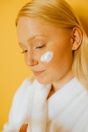 woman, facial cream, cheek, bathrobe, close-up, yellow background, skincare, beauty, blonde hair, white robe, applying cream