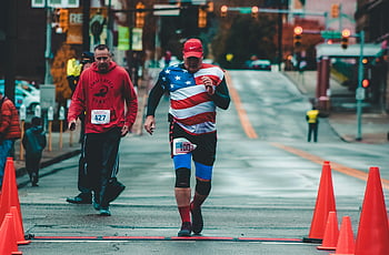 Městský maraton, WELING WV, cílová čára, běžci soutěží, dopravní kužely, Šedá cementová cesta, muž chůze, Košile americké vlajky, městský závod, pouliční závod, městská událost