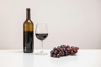 wine bottle, wine glass, grapes, white table, minimalist still life, red wine, table setting, still life photography, wine and grapes, simple composition, wine scene
