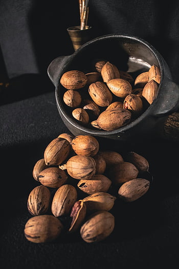 pecan nuts, unshelled pecans, rustic bowl, organic texture, dark surface, spilling pecans, nut shells, natural nuts, pecan shells, dark background, rustic setting