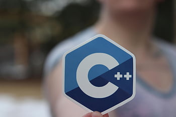 Logo C++, žena ruku, nálepka s držením, detail, rozmazané pozadí, programovací jazyk, šestiúhelníkový tvar, vývoj softwaru, technologie, kódování, osoba drží