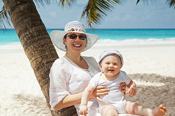 donna che tiene infantile, spiaggia, palme, giorno soleggiato, madre sorridente, bambino, rilassante, sabbia bianca, spiaggia tropicale, vacanza, tempo per la famiglia