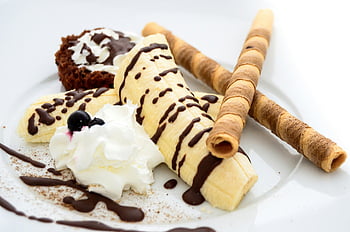 dessert di banana, pioggerellina al cioccolato, panna montata, bastoncini di wafer, torta marrone, piatto in ceramica bianca, avvicinamento, dolce, cioccolato, frustato, wafer