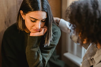følelsesmæssig støtte, trøstende ven, indendørs scene, Kvinde tapper skulderen, frustreret kvindelig, oplever sorg, Følelsesmæssig forbindelse, støttende gestus, indendørs komfort, kvindeligt venskab, følelsesmæssigt øjeblik