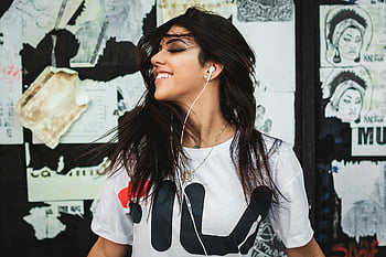 young woman, smiling, earphones, graffiti wall, white shirt, listening music, portrait, urban background, street art, casual style, headphones