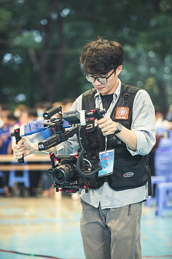 A camera operator, using a gimbal, stabilization, camera shots, outdoor event, videographer, professional filming, media equipment, sports event coverage, filming techniques.