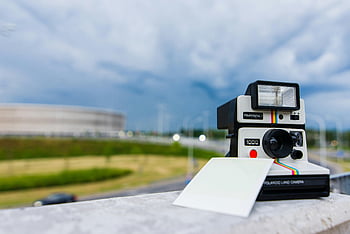 aparat Polaroid, natychmiastowa kamera, papier fotograficzny, fotografia miejska, Rozmyty pejzaż miejski, klasyczny aparat, fotografia plenerowa, zabytkowe kamery, natychmiastowe zdjęcie, tło miasta, Polaroid 1000