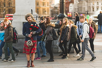 bagpipes, street performer, traditional music, kilt, public square, people walking, outdoor performance, urban scene, cultural event, city life, musical instrument