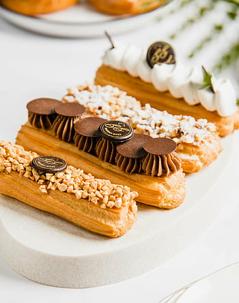 pasticcino, éclair artigianali, condimenti assortiti, piatto bianco, avvicinamento, delizioso, zucchero a velo, dischi di cioccolato, panna montata, noccioline, dolce
