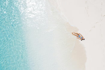 woman sunbathing, blue swimsuit, white sandy beach, turquoise water, serene beach, seashore, aerial view, relaxing beach, beach vacation, beach scene, woman lying on beach