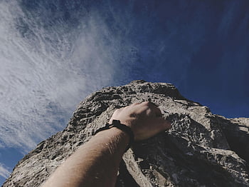 Hand des Kletterers, felsige Klippe, klarer blauer Himmel, Abenteuer, Klettern im Freien, Felsklettern, Handgriff, Bergsteigen, Outdoor-Abenteuer, Blick auf den Himmel, natürliche Landschaft