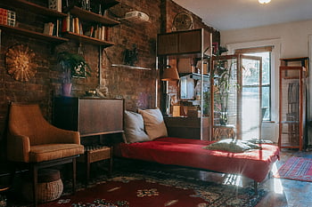classic bedroom, wooden furniture, antique carpets, vintage decor, cozy armchair, natural light, warm interior, inviting bedroom, red bedding, brick wall, potted plants