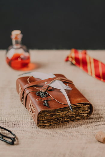 vintage book, white feather, brown textile, potion bottle, magical accents, still life composition, quill, key, red tie, glasses, cork