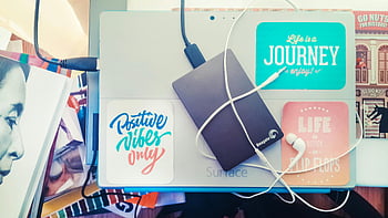 Schwarzes Seagate HDD, Graue Microsoft Surface Pro, Motivationsaufkleber, externe Festplatte, Kopfhörer, Buntes Schreibtisch, Ansicht von oben, Laptop, Nur positive Stimmung, Das Leben ist eine Reise, Das Leben ist besser in Flip -Flops