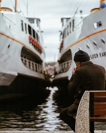 man sitting on bench, looking at ships, docked ships, Istanbul, sea view, waterfront, man smoking, bench by water, harbor scene, ferry boats, waterfront bench