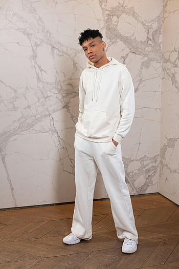 sebevědomý černoch, Neformální outfit, Bílá mikina, bílé kalhoty, Vnitřní nastavení, mladý muž, mramorové zdi, sebevědomá pozice, stylový vzhled, moderní móda, běžné civilní oblečení