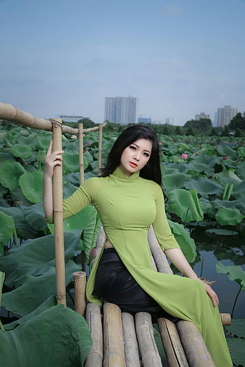Asian woman, green ao dai, lotus pond, cultural fashion, natural beauty, bamboo bridge, traditional dress, outdoor setting, Vietnamese culture, scenic landscape, lotus flowers