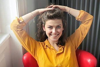 vrouw, geel shirt, button-up overhemd, Lange mouwen shirt, vrolijk, glimlachen, binnenshuis, handen achter het hoofd, rode stoel, natuurlijk licht, Informele stijl