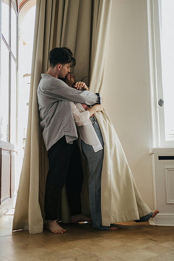 man hugging woman, loving couple, intimate embrace, by window, connection, affection, romantic moment, couple hugging, indoor scene, barefoot couple, curtains