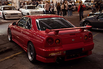 red Nissan Skyline, back view, custom livery, indoor car gathering, crowd, vibrant red, car display, rear view, Nissan Skyline, custom paint, car event