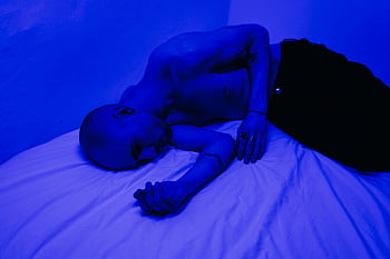Uomo sdraiato sul letto, camera illuminata blu, solitudine, introspezione, uomo sul letto, illuminazione blu, umore contemplativo, Posa rilassata, Scena indoor, spazio personale, atmosfera calma