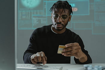 man hacking, bank card, typing on keyboard, sitting in front of computer, man with glasses, computer screen, online security, cybercrime, financial fraud, data breach, digital crime