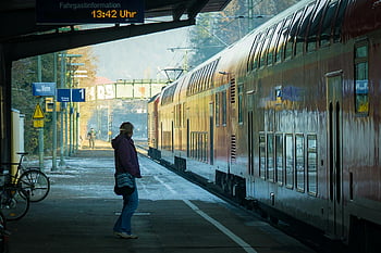 person near train, train coaches, sunny outdoor station, waiting beside train, train station, outdoor station, sunny day, train platform, person waiting, train travel, station platform