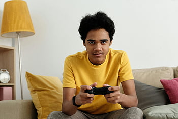 Teen hrající videohry, žluté tričko, Vnitřní nastavení, gauč, řadič videoher, příležitostné hraní, obývací pokoj, pohodlné nastavení, Zaměřený hráč, uvolněné prostředí, domácí zábava