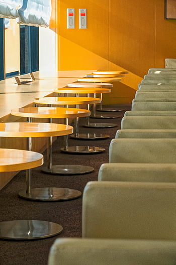 tavoli rotondi di legno giallo, area di attesa moderna, Narita Giappone, stanza illuminata dal sole, file di posti, area salotto interno, design contemporaneo, lounge dell'aeroporto, sedie comode, luce naturale, interior design