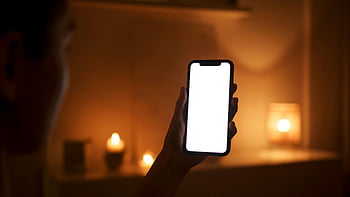 스마트 폰을 들고있는 사람, 암실, 촛불 방, 아늑한 설정, 현대 기술, 따뜻한 설정, 스마트 폰 사용, 실내 장면, 주변 조명, 편안한 분위기, 저녁 분위기