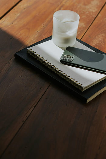 minimalist desk setup, smartphone, notebook, candle, warm light, productivity, simple desk scene, wooden desk, spiral notebook, minimalist workspace, cozy workspace