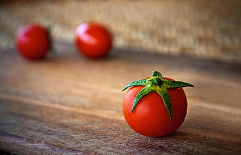 cherry tomatoes, wooden table, vibrant tomatoes, rustic surface, freshness, organic appeal, close-up, red tomatoes, green stems, natural produce, food photography