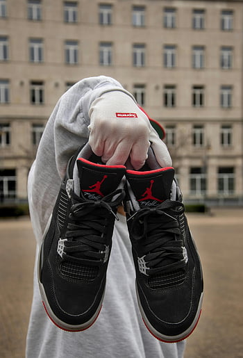Grå langermet skjorte, nike sneakers, urbane stil, Nærbilde joggesko, utendørs bilde, bygge bakgrunn, Supreme hansker, svarte joggesko, Røde aksenter, gaten mote, person som holder joggesko