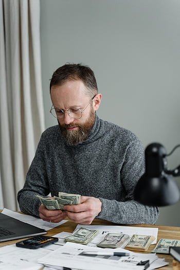 vousatý muž, šedý svetr, Počítání dolarů, Nastavení kanceláře, hotovost, papíry, laptop, lavice, Finanční řízení, Počítání peněz, brýle