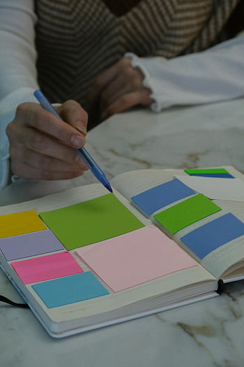 barevný poznámkový blok, notebook, samolepící papírky, mramorový stůl, ruku s perem, Barevné lepkavé poznámky, otevřený zápisník, psaní, plánování, organizace, nastavení stolu