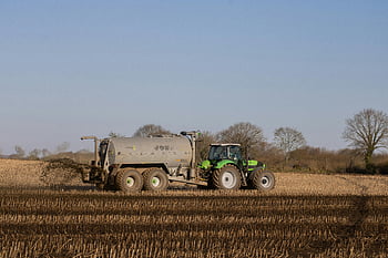 tractor, fertilizing, brown field, green tractor, spreading fertilizer, freshly plowed farmland, clear sky, agricultural equipment, farming, rural scene, tractor tank