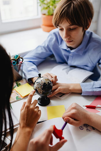 Studenten studieren Globus, Kinder erkunden den Globus, Geographie lernen, Gruppenstudie, Schreibtischstudie, Bildungsaktivität, kollaboratives Lernen, Aktivität im Klassenzimmer, Geographiestunde, gemeinsam lernen, Globus-Erkundung