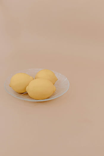 lemons, glass plate, beige surface, minimalist look, fresh lemons, three lemons, beige background, fruit display, simple composition, still life, citrus fruits