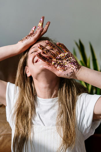 woman, white crew neck shirt, glitter-covered hands, celebrating, indoors, joyfully, red and white floral, heart shaped cake, long hair, plant background, festive mood