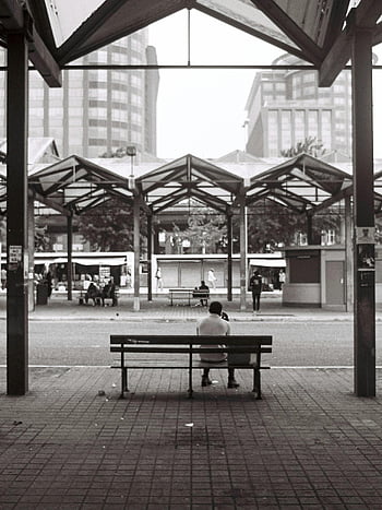 person sitting, bench, bus terminal, Lisbon, traveler, modern architecture, terminal, urban scene, public transportation, cityscape, black and white