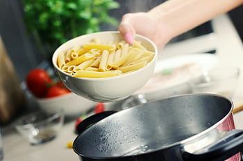 person holding bowl, white ceramic bowl, penne pasta, boiling pasta, stainless steel pot, kitchen scene, cooking process, fresh ingredients, food preparation, home cooking, pasta dish