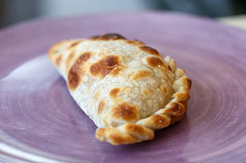 empanada, detailní záběr, čerstvě upečený, Argentinská empanada, fialová deska, autentická textura, fotografování potravin, pečené pečivo, kulinářské umění, tradiční kuchyně, jídlo zblízka